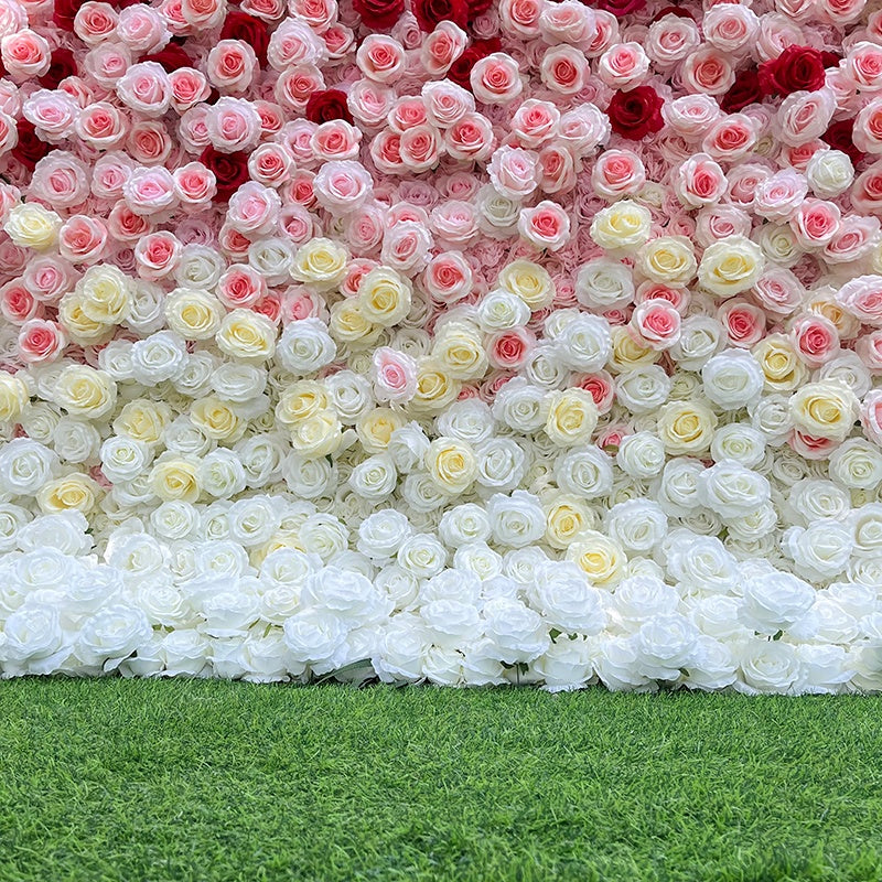 Wall of artificial flowers transitioning from pink to white on a grassy background
