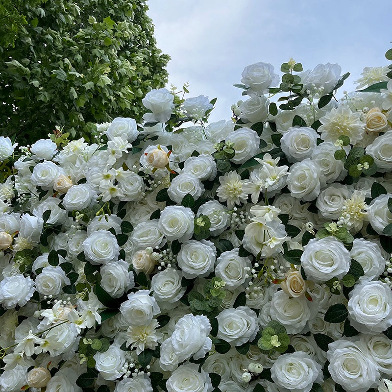 Wall of white and light-colored flowers with greenery against a clear sky.